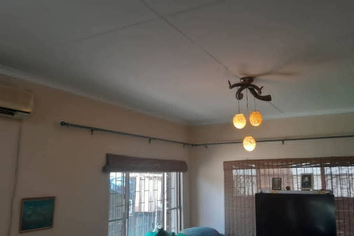 A living room featuring a ceiling fan, wall-mounted air conditioning unit, and security bars on the windows.