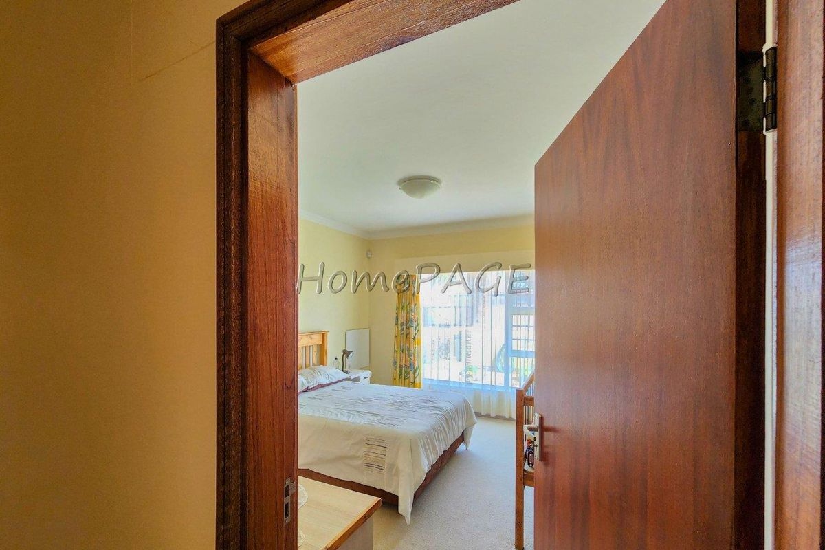 A view through a wooden door frame into a bedroom featuring large windows and neutral carpeting.