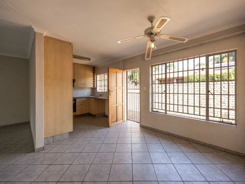 Open-plan living area featuring tiled flooring, a ceiling fan, and an adjoining kitchen with built-in cabinetry and security bars on the windows.