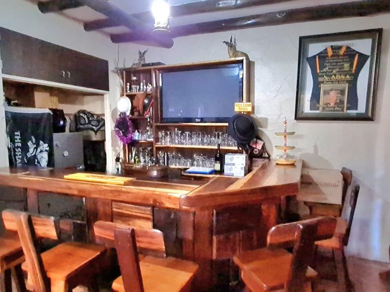 A rustic home bar area featuring a custom wooden bar counter, built-in shelving, and exposed timber ceiling beams.