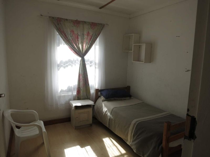 A compact bedroom featuring laminate flooring and built-in wall shelving, requiring cosmetic updates to the walls and ceiling to improve its overall condition.