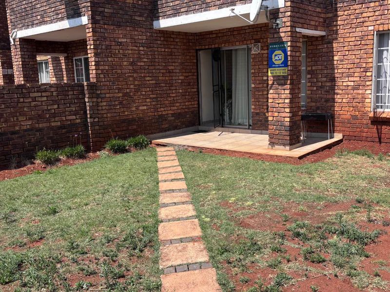 Rear view of an apartment featuring a brick facade, a small tiled patio area, and a private garden space with a paved walkway.