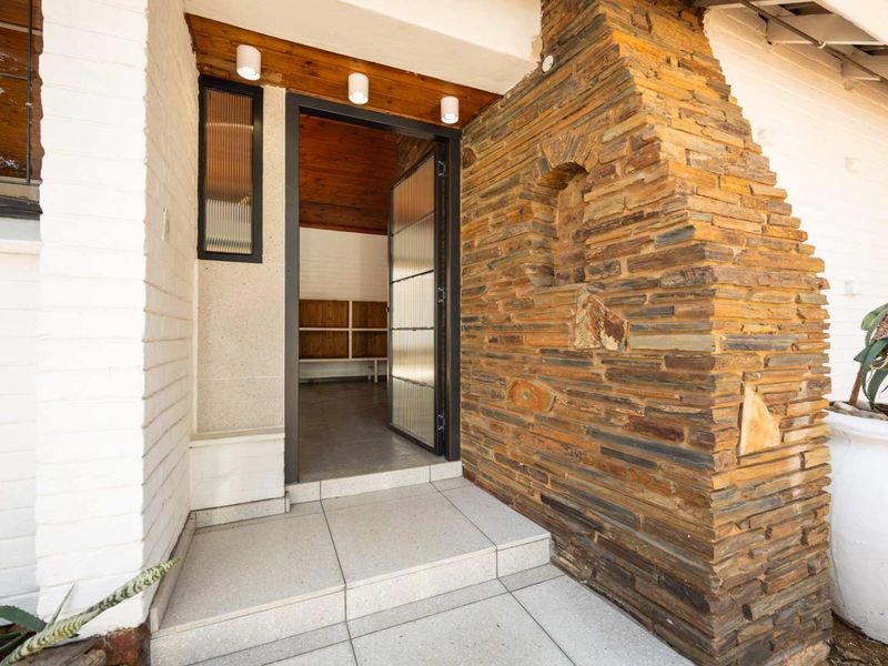 A welcoming entrance featuring a striking stone-clad feature wall, tiled porch, and a modern fluted glass door under a timber-lined ceiling.