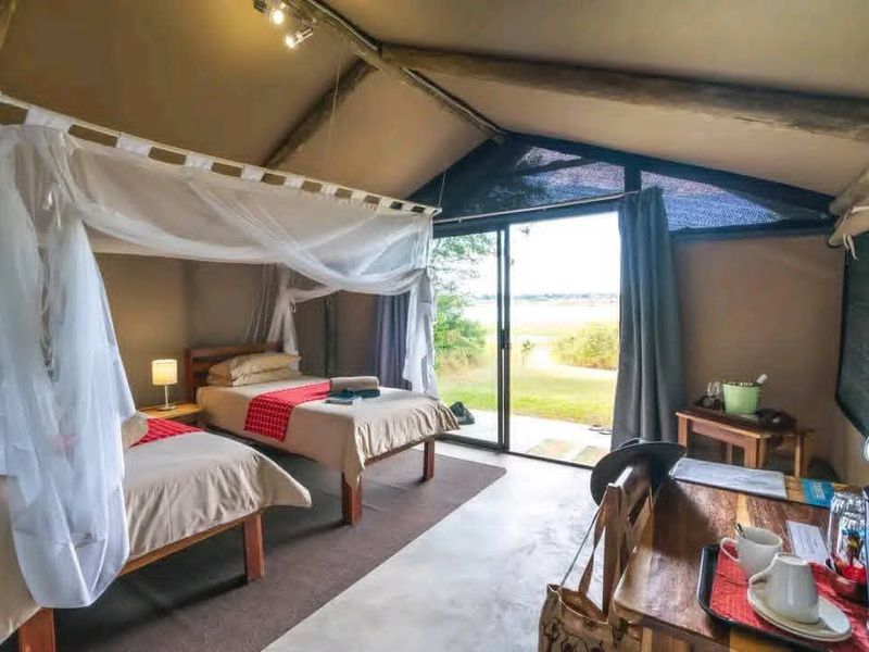 A well-maintained safari-style bedroom featuring exposed timber rafters, canvas walls, and a sliding glass door providing direct access to the outdoor landscape.