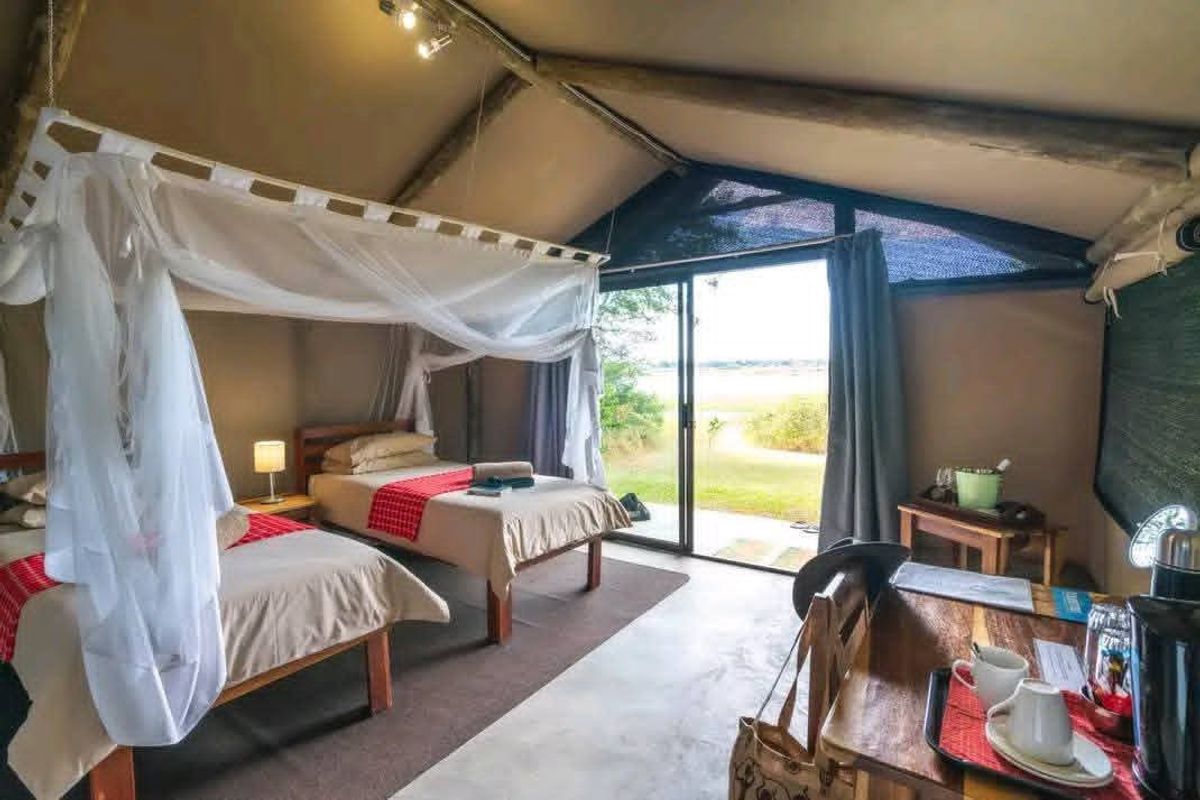 A well-maintained safari-style bedroom featuring exposed timber rafters, canvas walls, and a sliding glass door providing direct access to the outdoor landscape.