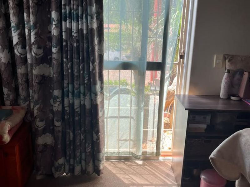 A bedroom featuring a sliding glass door with an integrated security gate, providing access to the exterior and allowing natural light into the space.