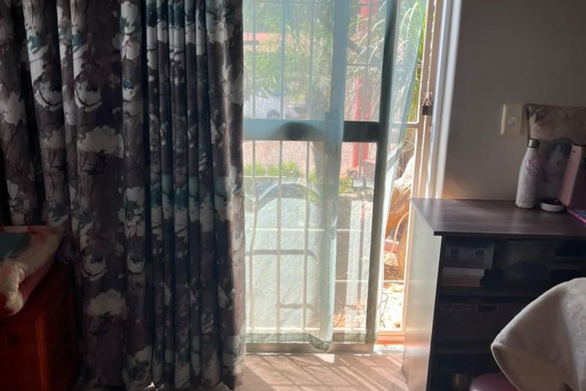 A bedroom featuring a sliding glass door with an integrated security gate, providing access to the exterior and allowing natural light into the space.