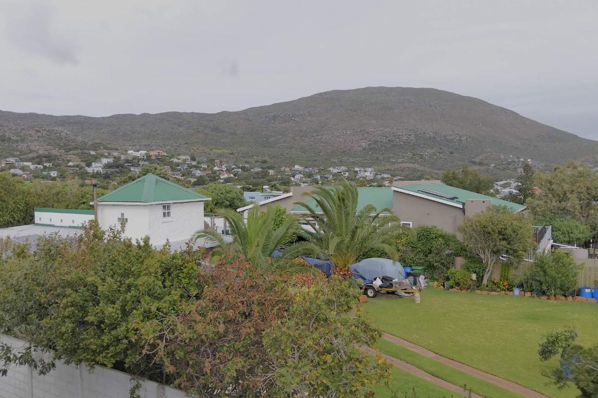 Aerial view of the property grounds featuring a large lawn, established garden, and surrounding residential neighbourhood with mountain views.