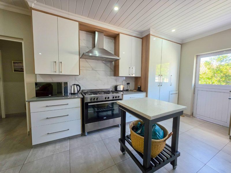 Modern kitchen featuring white cabinetry, gas stove with extractor fan, marble-look splashback, and tiled flooring with a tongue and groove ceiling.
