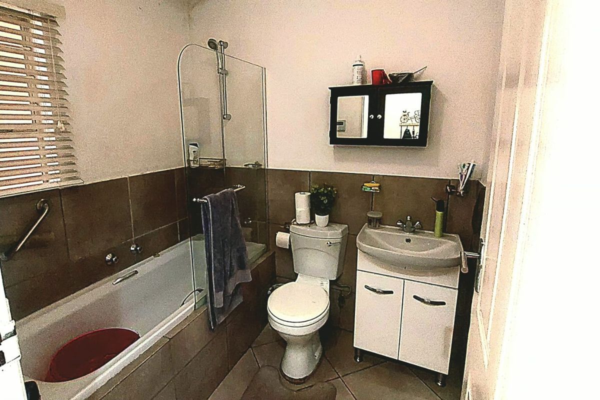 A functional bathroom featuring a bathtub with a glass shower screen, a toilet, and a vanity basin with storage.