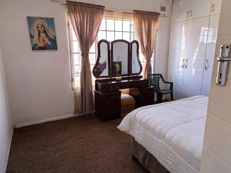 A bedroom featuring built-in cupboards, a large window with curtains, and carpeted flooring.