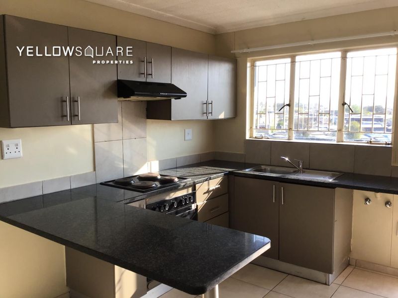 A functional kitchen featuring dark cabinetry, granite countertops, an integrated hob with extractor fan, and a stainless steel sink with natural light.
