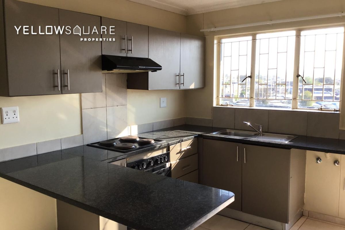 A functional kitchen featuring dark cabinetry, granite countertops, an integrated hob with extractor fan, and a stainless steel sink with natural light.