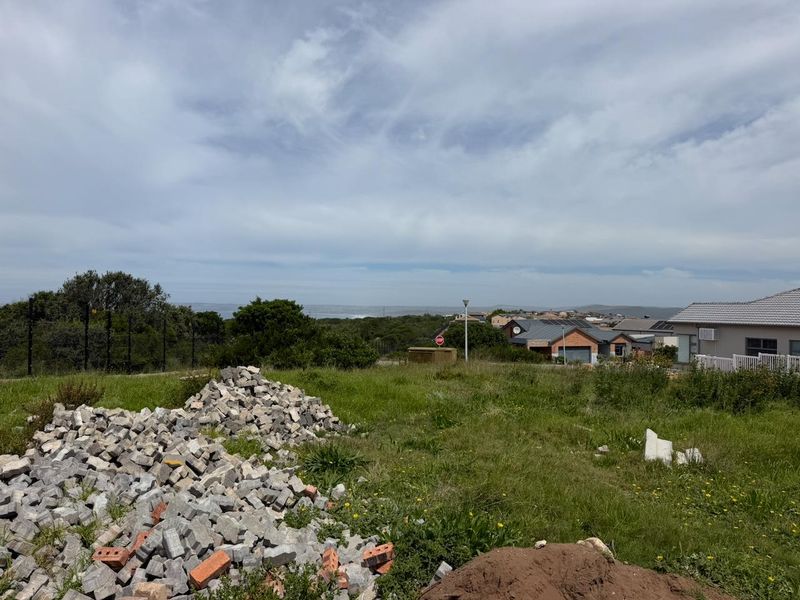 A vacant residential plot featuring a gentle slope, existing electric fencing, and distant coastal views, currently containing construction debris and overgrown grass.