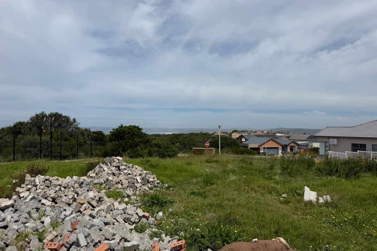 A vacant residential plot featuring a gentle slope, existing electric fencing, and distant coastal views, currently containing construction debris and overgrown grass.