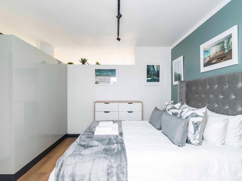 A well-maintained bedroom featuring modern built-in cupboards, laminate flooring, and contemporary track lighting with a stylish accent wall.