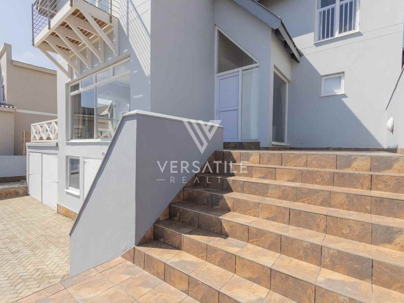 Front exterior view of the property featuring a tiled staircase leading to the entrance, paved driveway, and a metal staircase to the upper level.