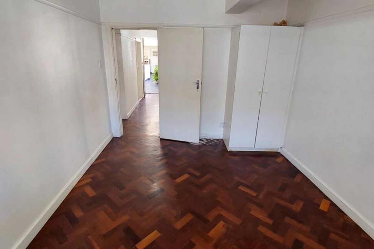 A bedroom featuring classic herringbone parquet flooring, built-in wardrobe storage, and a neutral interior finish, leading into a connecting hallway.