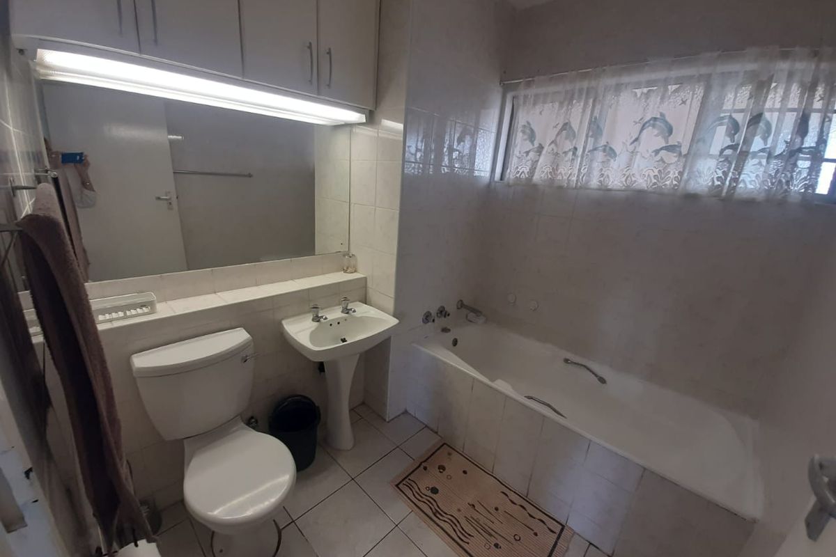 A functional bathroom featuring a white bathtub, pedestal sink, toilet, and wall-mounted storage cabinetry with integrated lighting.