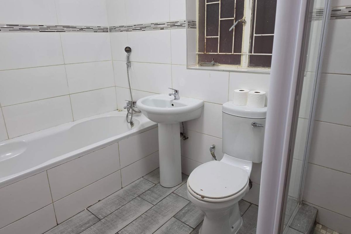 A functional bathroom featuring a white bathtub, pedestal basin, and toilet with tiled walls and flooring.
