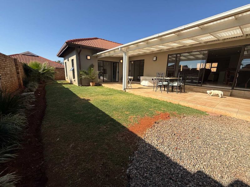 A rear view of the property featuring a covered tiled patio, sliding glass doors, and a private garden with a brick boundary wall.