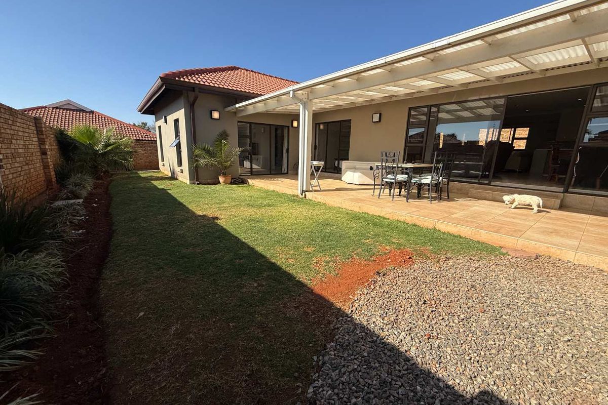 A rear view of the property featuring a covered tiled patio, sliding glass doors, and a private garden with a brick boundary wall.
