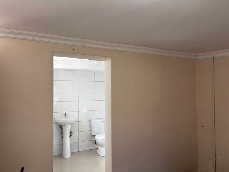 A functional bathroom featuring a pedestal washbasin and toilet, finished with white wall tiles and neutral wall paint.