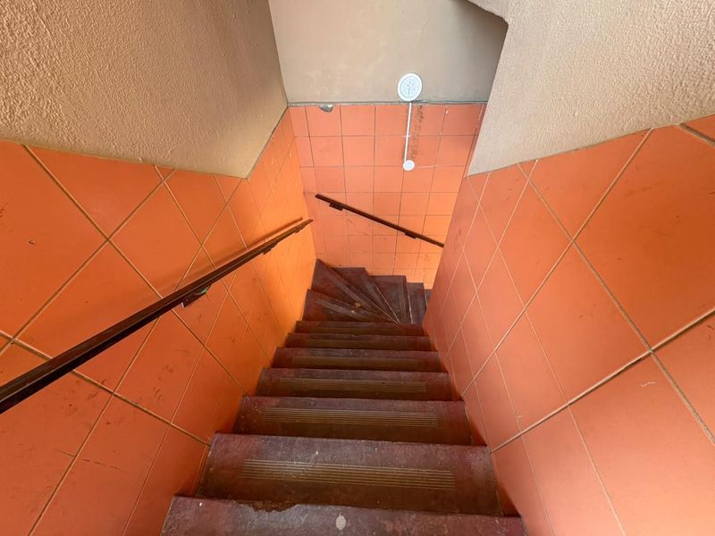 A functional staircase featuring orange tiled wall cladding and a metal handrail, showing signs of age and wear.