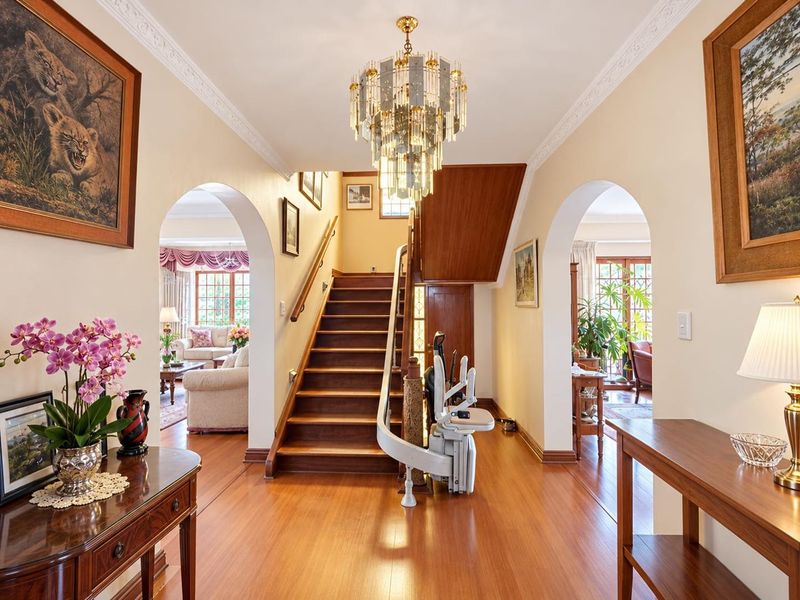 Welcoming entrance hall featuring a grand wooden staircase with a fitted stairlift, elegant arched doorways, crown molding, and a sophisticated crystal chandelier.