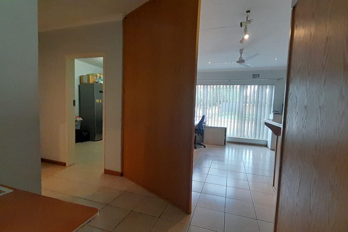 A view through a doorway into a tiled living area featuring a large wooden partition, ceiling fan, and vertical blinds.