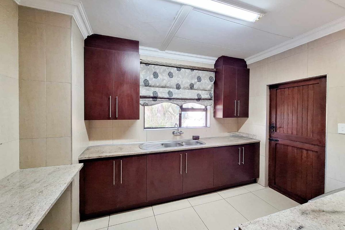 A functional kitchen featuring dark wood cabinetry, granite countertops, a double-basin sink, and tiled flooring with neutral wall tiles.