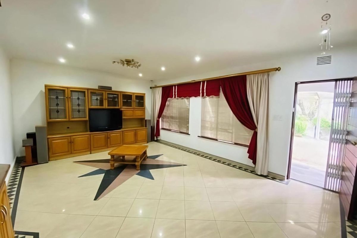 Spacious living room featuring tiled flooring with decorative inlay, built-in wooden cabinetry, and direct access to the exterior through a security gate.