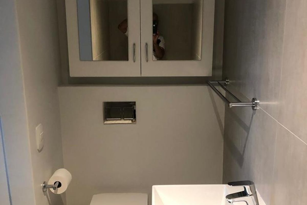 A modern guest bathroom featuring a wall-mounted toilet, a sleek basin with a chrome mixer tap, and a mirrored wall cabinet.