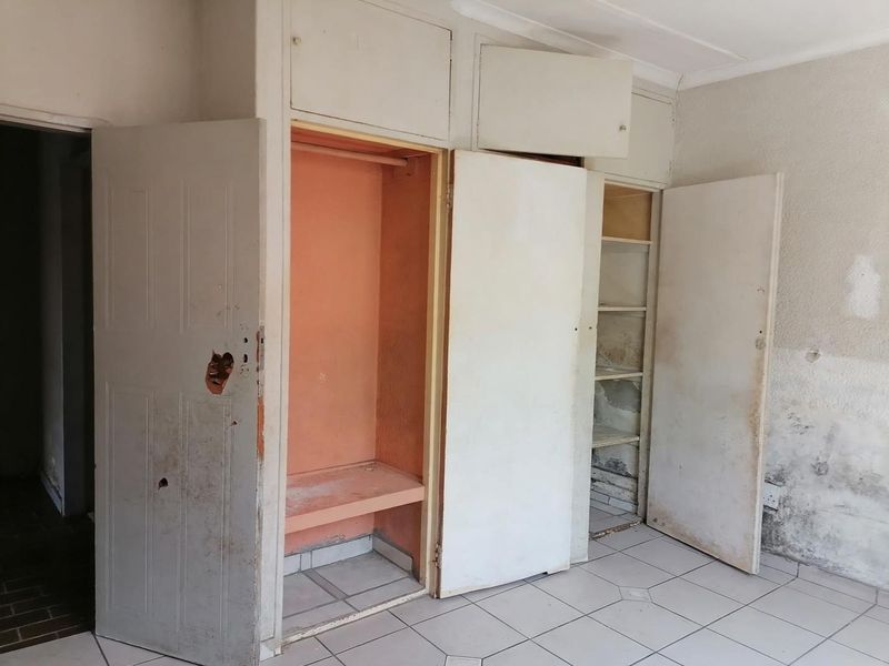 An empty bedroom featuring built-in cupboards and tiled flooring, currently requiring significant maintenance and cosmetic repairs to the walls and cabinetry.