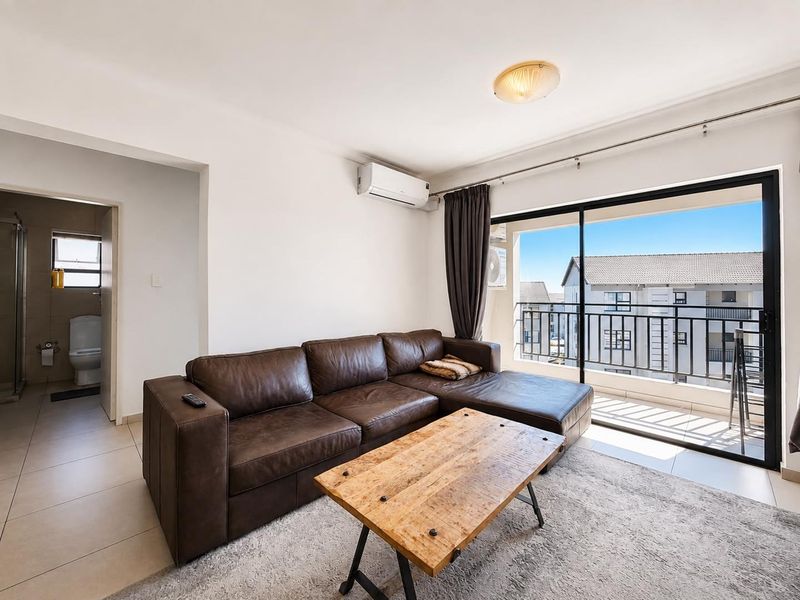 A bright living room featuring tiled floors, a wall-mounted air conditioning unit, and large sliding glass doors leading to an outdoor balcony.