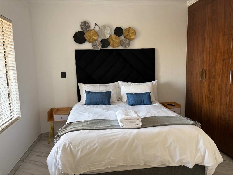 A well-maintained bedroom featuring built-in wooden cupboards, tiled flooring, and venetian blinds, offering a clean and functional living space.