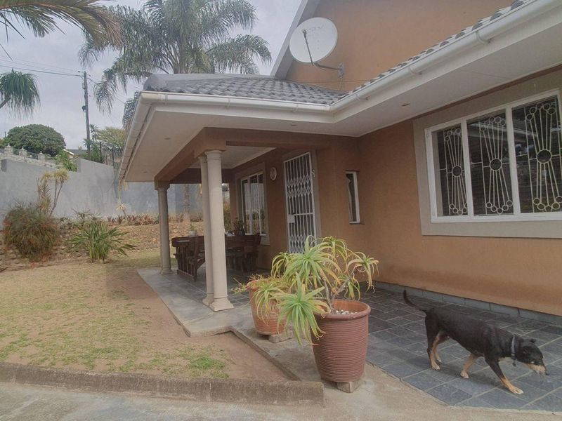 A rear view of the house featuring a covered tiled patio, concrete columns, and secure window bars, overlooking a landscaped garden area.
