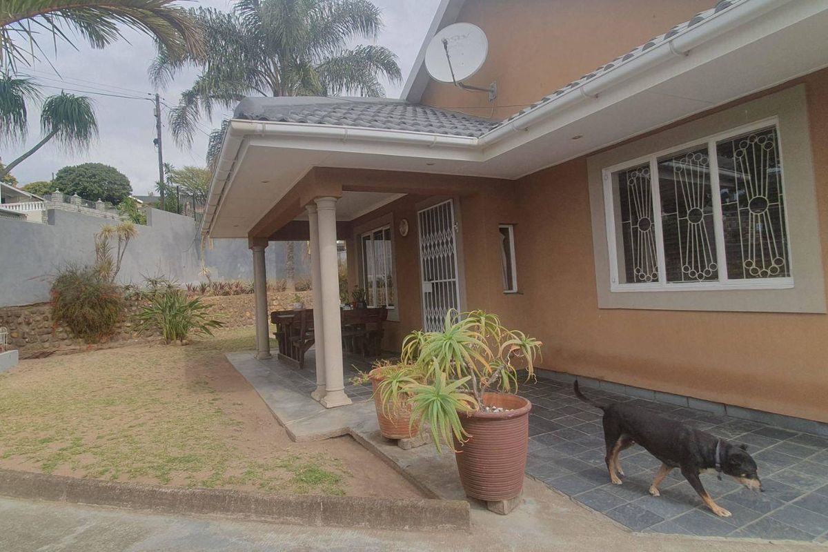 A rear view of the house featuring a covered tiled patio, concrete columns, and secure window bars, overlooking a landscaped garden area.