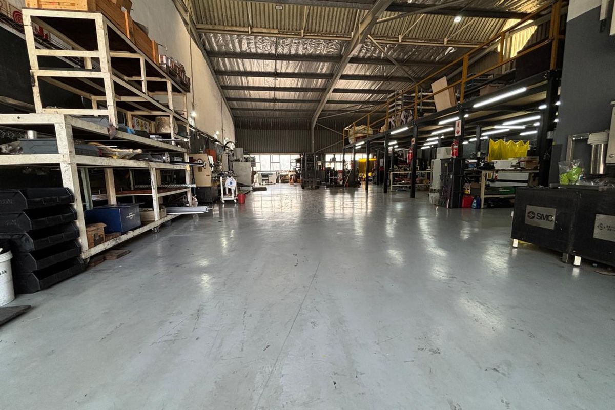 Spacious industrial warehouse featuring high ceilings with exposed steel trusses, durable epoxy flooring, and integrated mezzanine storage levels.