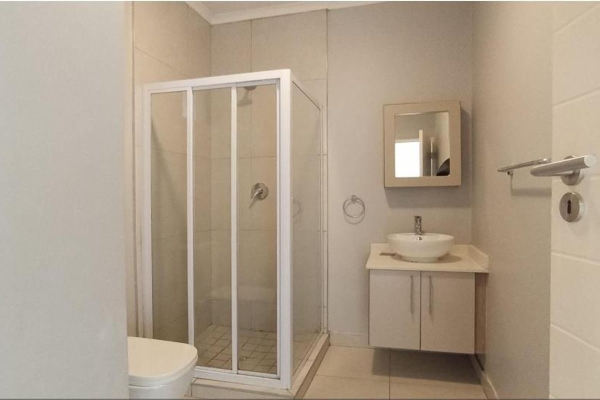 A clean, modern bathroom featuring a glass-enclosed shower, a vanity with a vessel sink, and neutral wall tiling.