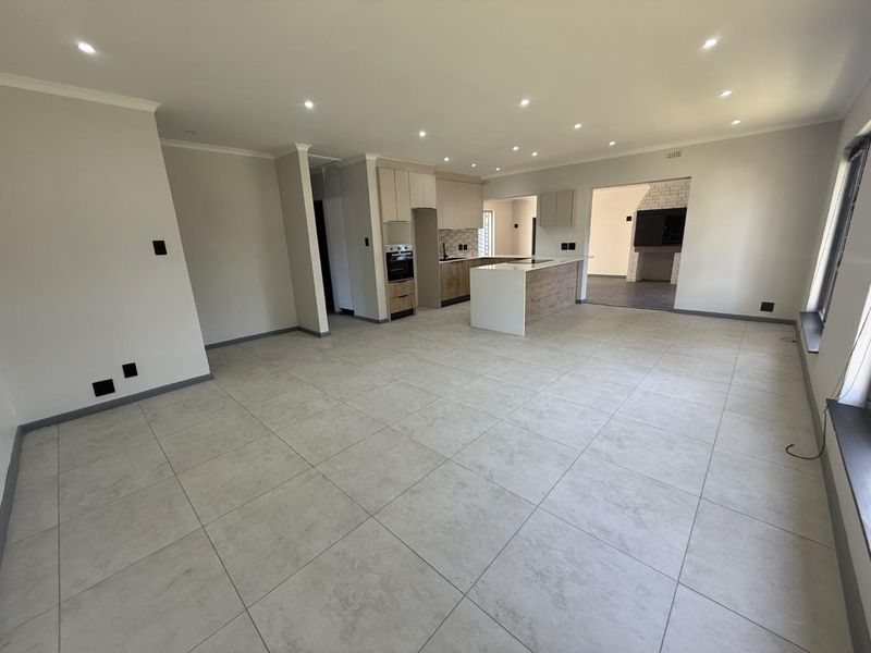 Spacious open-plan living area featuring modern tiled flooring, recessed lighting, and a contemporary kitchen with a central island and built-in appliances.