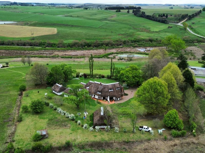 Aerial view of a rural property featuring a main house with a traditional thatched roof, surrounding outbuildings, and expansive landscaped grounds.