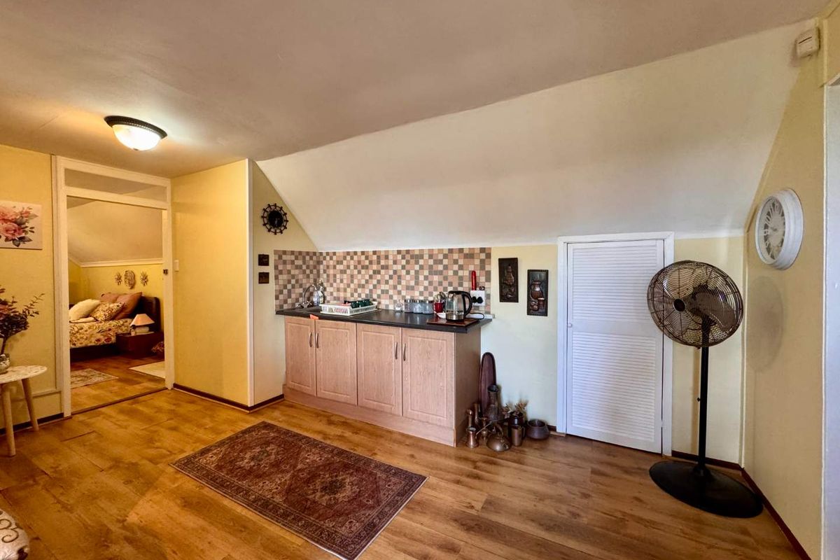 A compact kitchenette area featuring light wood cabinetry, a tiled backsplash, and laminate flooring, situated within an open-plan living space.