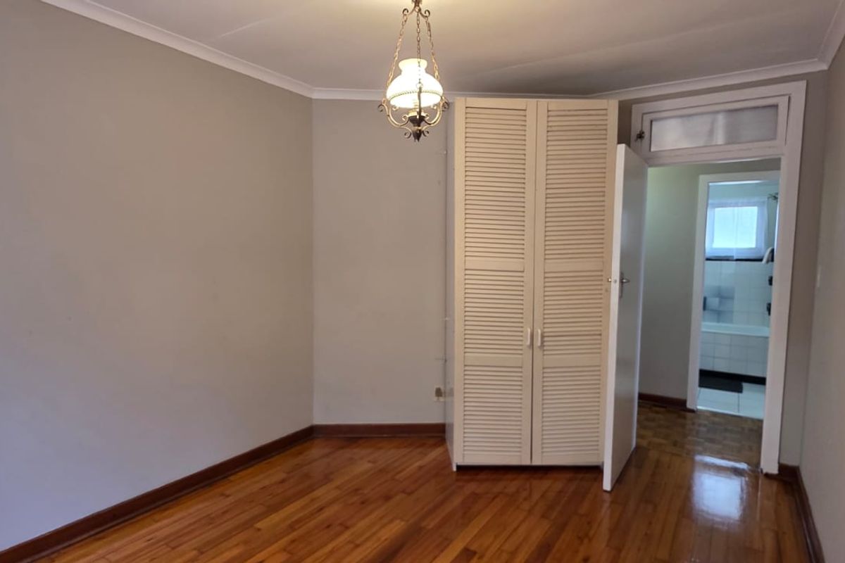 A bright, empty bedroom featuring polished hardwood flooring, a built-in cupboard, and direct access to an adjoining bathroom.