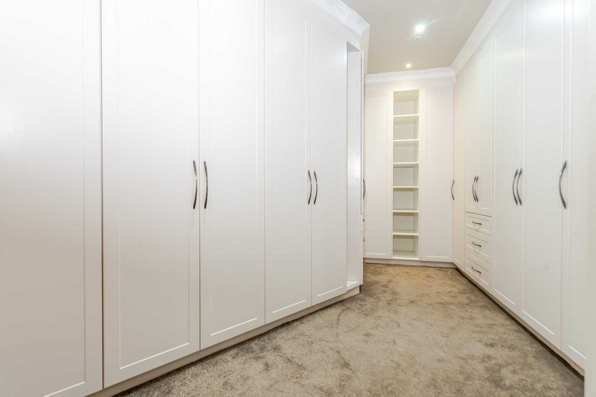 A spacious walk-in dressing room featuring extensive floor-to-ceiling built-in cabinetry, integrated shelving, and plush carpeting.