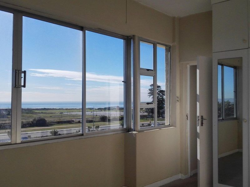 A bright, empty bedroom featuring built-in cupboards with mirrored doors and large sliding windows offering expansive coastal and landscape views.