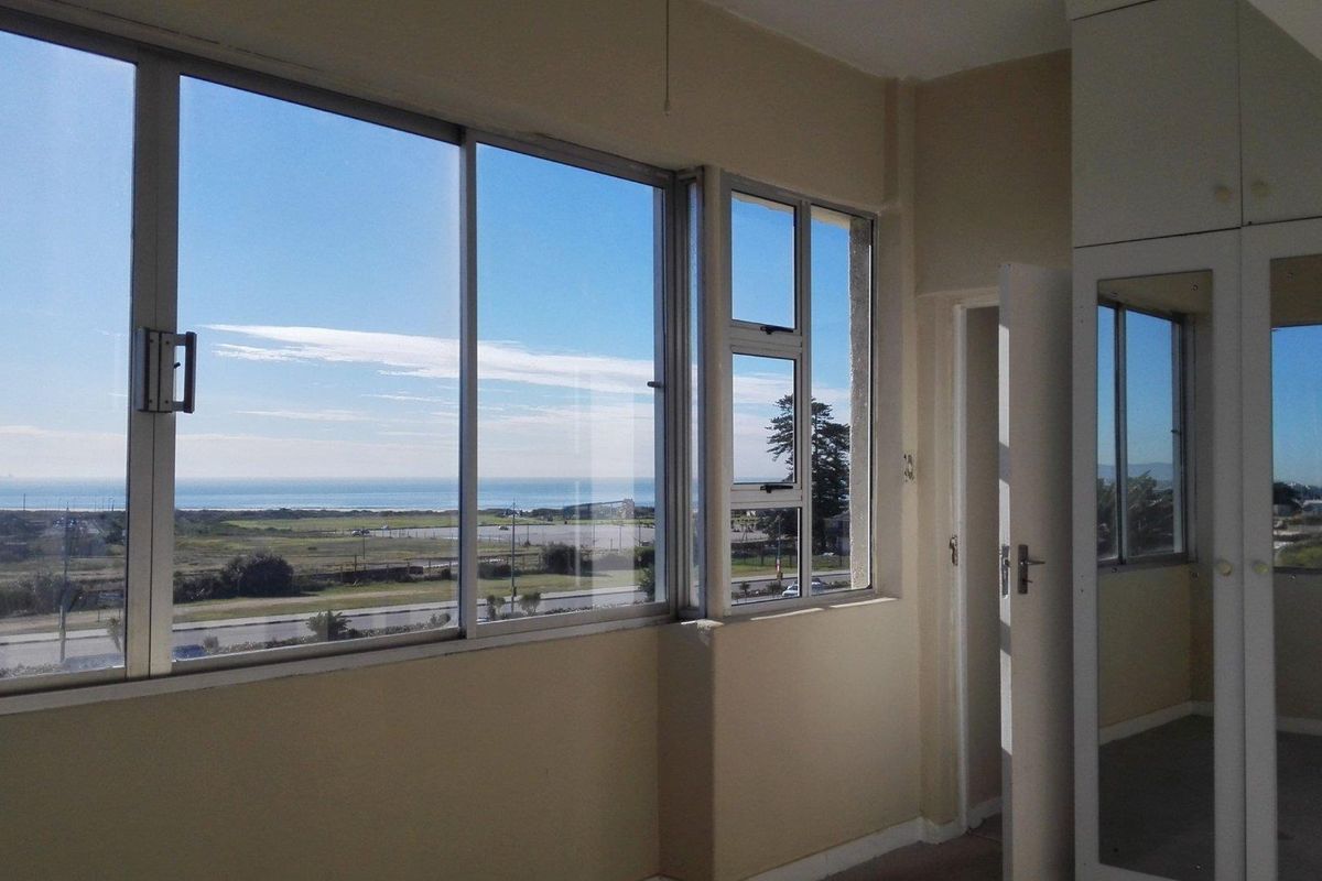 A bright, empty bedroom featuring built-in cupboards with mirrored doors and large sliding windows offering expansive coastal and landscape views.