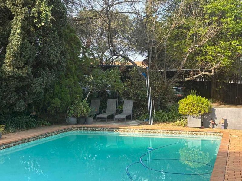 A private outdoor swimming pool area featuring brick paving and established garden surroundings.