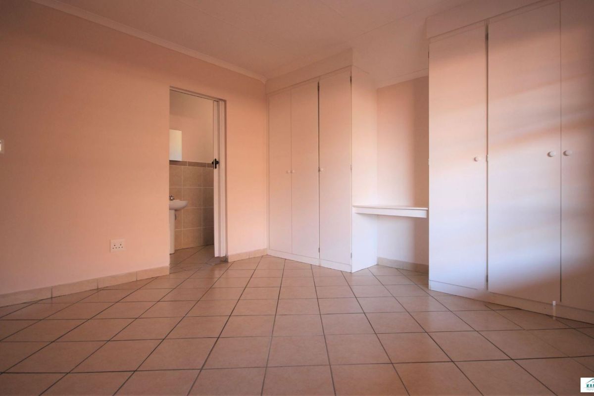 A spacious, empty bedroom featuring neutral tiled flooring, ample built-in cupboard storage, and direct access to an en-suite bathroom.