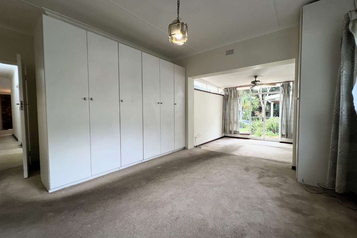 Spacious bedroom featuring extensive built-in cabinetry, neutral carpeting, and a connected sunroom area with direct access to the garden.